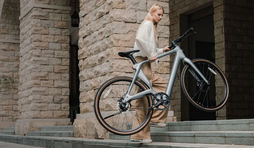 A woman effortlessly lifts a Fiido Air lightweight electric bike up the stairs.