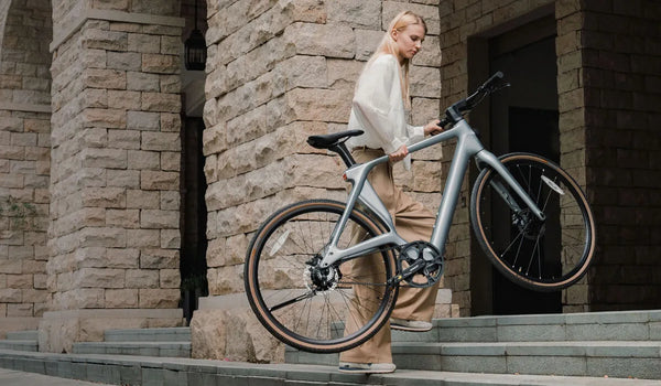 A woman effortlessly lifts a Fiido Air lightweight electric bike up the stairs.