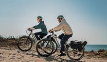 A couple is riding their Fiido Nomads Pro e-bikes along a mountain road.