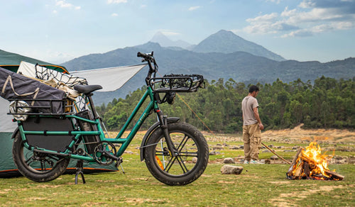 Fiido T2 electric cargo bike loaded with camping gear at a mountain campsite beside a tent and campfire.